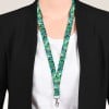 Das Bild zeigt eine Person, die einen schwarzen Blazer über einem weißen Hemd trägt. Sie tragen ein buntes Lanyard mit einem Muster aus Grünpflanzen und Blumen, das an einem Clip befestigt ist.