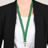 Das Bild zeigt eine Person, die einen schwarzen Blazer über einem weißen Hemd trägt, mit einem grünen Lanyard, das um ihren Hals hängt. Das Lanyard hat unten einen Clip, wahrscheinlich zum Halten eines Ausweises oder Abzeichens.