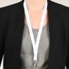 Das Bild zeigt eine Person, die einen schwarzen Blazer über einem grauen Oberteil trägt, mit einem weißen Umhängeband, das um den Hals hängt. Das Umhängeband hält ein transparentes Namensschild oder einen Ausweis.