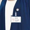 Das Bild zeigt einen Besucher-Namensschild, das an der Kleidung einer Person befestigt ist. Das Schild trägt den Namen 'E. Smith' und den Titel 'Ingenieur.' Es zeigt außerdem einen Anstecker mit dem Avery-Logo.