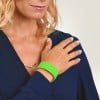 Das Bild zeigt eine Frau, die eine marineblaue Bluse und ein grünes Armband an ihrer Hand trägt. Sie hält ihre Hand an ihre Schulter, und ihr Haar ist in lockeren Wellen gestylt. Der Hintergrund ist ein leichter Farbverlauf.