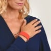 Das Bild zeigt eine Frau mit blonden Haaren, die eine dunkelblaue Bluse trägt und eine Hand auf ihrer Schulter platziert hat. Sie hat eine dünne Halskette und trägt ein orangefarbenes Armband am Handgelenk.