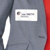 Das Bild zeigt eine Person, die eine graue Anzugsjacke trägt, an der ein Namensschild mit der Aufschrift 'Julia SMITH Marketing' befestigt ist.
