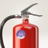 Das Bild zeigt einen roten Feuerlöscher mit einer Düse, einem Druckmesser und einem Etikett, das das Datum der nächsten Inspektion angibt.