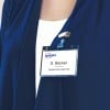 Das Bild zeigt ein Namensschild, das an der Kleidung einer Person befestigt ist und den Namen S. Becker zusammen mit dem Titel Marketing Director anzeigt. Das Schild wird von einem Clip gehalten, ist transparent mit blauen Akzenten, und die Person trägt ein dunkelblaues Kleidungsstück.