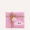 Eine wunderschön verpackte rosa Geschenkbox, verziert mit Schnur und einer kleinen Blume. Sie hat ein Etikett mit dem Namen 'Anna' darauf.