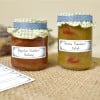 Das Bild zeigt zwei Gläser mit hausgemachten Würzmitteln. Ein Glas enthält 'Paprika-Zucchini-Chutney', während das andere 'Grüne Tomaten-Relish' enthält. Beide Gläser sind mit dekorativen Deckeln versehen und stehen auf einer Sackleinen-Oberfläche.