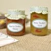 Das Bild zeigt zwei Gläser mit Eingemachtem. Ein Glas enthält Paprika-Zucchini-Chutney und das andere enthält grünes Tomaten-Relish. Beide Gläser sind mit karierten Stoffdeckeln versehen.