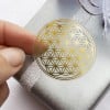 Das Bild zeigt eine Nahaufnahme einer Hand, die einen goldenen Aufkleber mit Blumenmuster auf eine silberne Geschenkbox drückt, die mit einem glitzernden Band verziert ist.