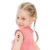 Ein junges Mädchen mit einem spielerischen Ausdruck schaut zurück und zeigt temporäre Tattoos auf ihrem Arm. Sie hat hellblondes Haar, das zu Zöpfen geflochten ist, und trägt ein rosa Shirt.