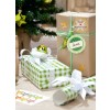 Das Bild zeigt Weihnachtsgeschenke, die in dekoratives Papier eingewickelt sind, mit einem kleinen Weihnachtsbaum im Hintergrund. Die Geschenke haben grüne und weiße Muster, und eines ist mit "Anna" beschriftet. Es gibt goldene Verzierungen und einen Stern auf den Geschenken, die eine festliche Atmosphäre schaffen.